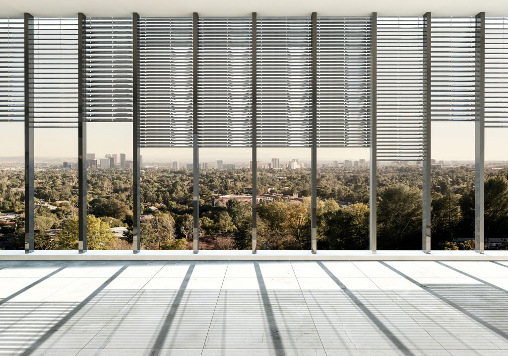 Large spacious unfurnished room with glass window wall and Venetian blinds overlooking a city with greenery and trees. 3d Rendering.